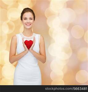 happiness, health, charity and love concept - smiling woman in white dress with red heart over golden lights background