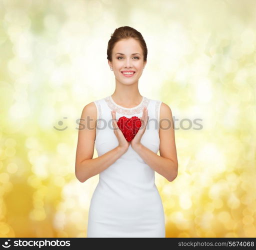 happiness, health, charity and love concept - smiling woman in white dress with red heart over golden lights background