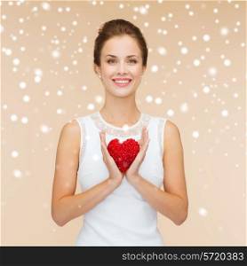 happiness, health, charity and love concept - smiling woman in white dress with red heart over beige background over beige background and snow