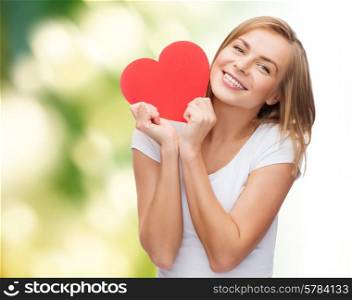happiness, health, people, holidays and love concept - smiling young woman in white t-shirt holding red heart over green background