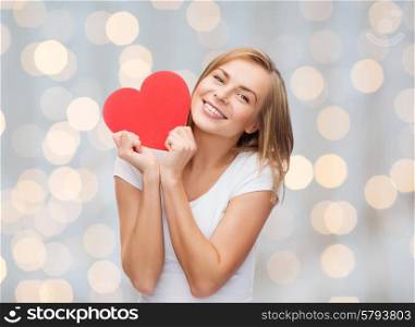 happiness, health, people, holidays and love concept - smiling young woman in white t-shirt holding red heart over lights background