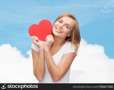 happiness, health, people, holidays and love concept - smiling young woman in white t-shirt holding red heart over blue sky with cloud background