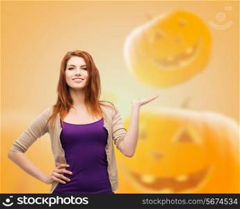 happiness, holidays and people concept - smiling teenage girl in casual clothes holding something on her palm over halloween pumpkins background