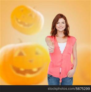 happiness, holidays and people concept - smiling teenage girl in casual clothes showing thumbs up over halloween pumpkins background