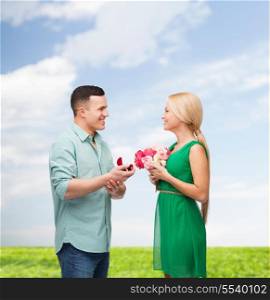 happiness, holidays, celebration and couple concept - smiling couple with flower bouquet and ring in a box