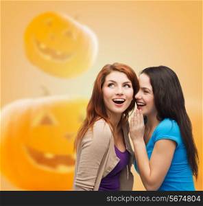 happiness, holidays, firendship and people concept - smiling teenage girls gossiping over halloween pumpkins background