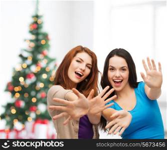 happiness, holidays, friendship and people concept - smiling teenage girls having fun over living room and christmas tree background