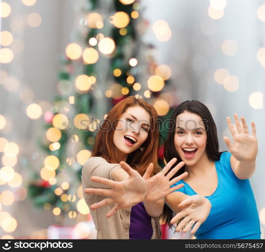 happiness, holidays, friendship and people concept - smiling teenage girls having fun over christmas tree background