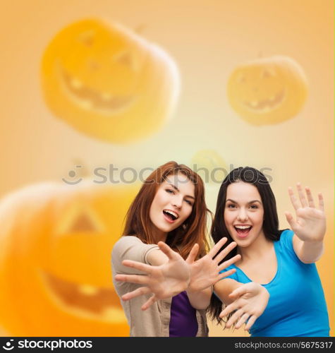 happiness, holidays, friendship and people concept - smiling teenage girls having fun over halloween pumpkins background