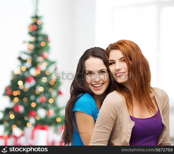 happiness, holidays, friendship and people concept - smiling teenage girls hugging over living room and christmas tree background