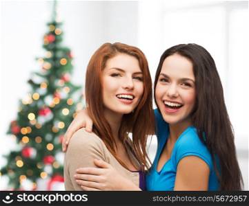 happiness, holidays, friendship and people concept - smiling teenage girls hugging over living room and christmas tree background