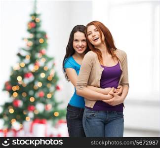 happiness, holidays, friendship and people concept - smiling teenage girls hugging over living room and christmas tree background