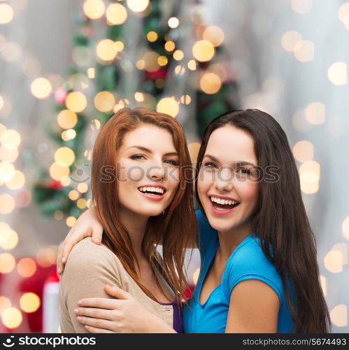 happiness, holidays, friendship and people concept - smiling teenage girls hugging over christmas tree background