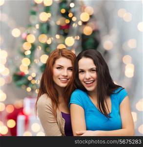 happiness, holidays, friendship and people concept - smiling teenage girls hugging over christmas tree background