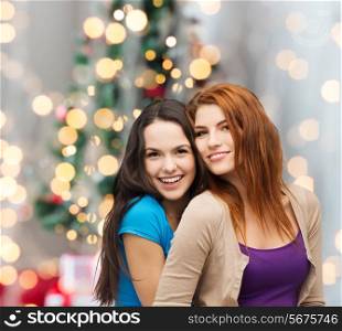 happiness, holidays, friendship and people concept - smiling teenage girls hugging over christmas tree background