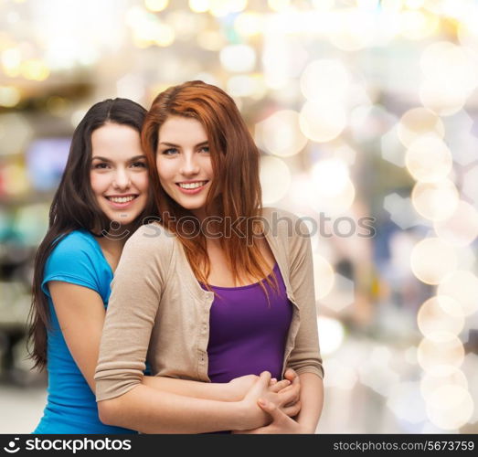 happiness, holidays, friendship and people concept - smiling teenage girls hugging over lights background