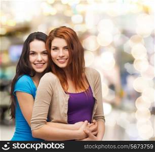 happiness, holidays, friendship and people concept - smiling teenage girls hugging over lights background