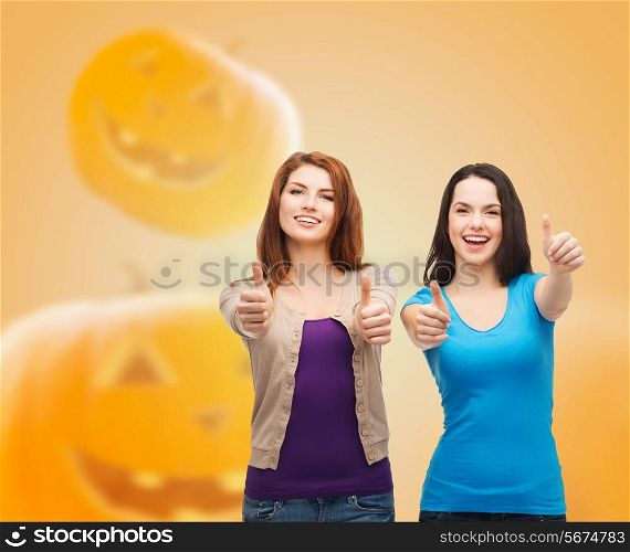 happiness, holidays, friendship, gesture and people concept - smiling teenage girls showing thumbs up over halloween pumpkins background