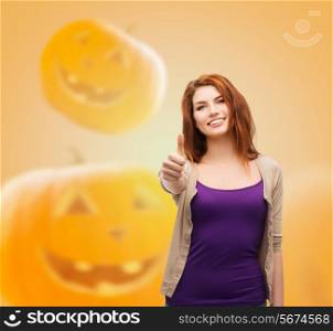 happiness, holidays, gesture and people concept - smiling teenage girl showing thumbs up over halloween pumpkins background