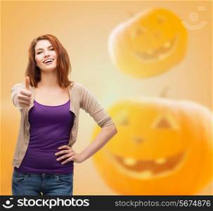 happiness, holidays, gesture and people concept - smiling teenage girl showing thumbs up over halloween pumpkins background