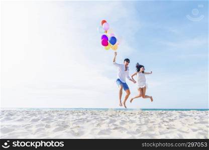Happiness lover couple holding colorful balloons and jumping with smile on the tropical beach in sunny day.