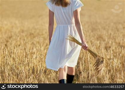 happiness, nature, summer holidays, vacation and people concept - close up of young woman with cereal spikelets walking on field