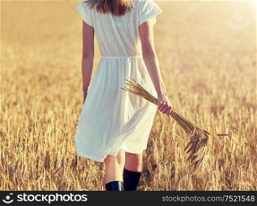 happiness, nature, summer holidays, vacation and people concept - close up of young woman with cereal spikelets walking on field. young woman with cereal spikelets walking on field