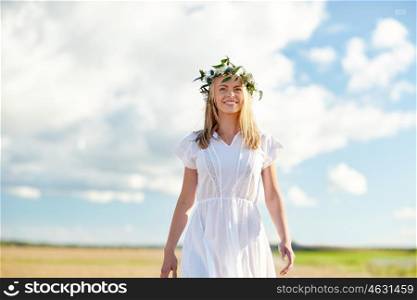 happiness, nature, summer holidays, vacation and people concept - happy smiling young woman or teenage girl in wreath of flowers and white dress at countryside