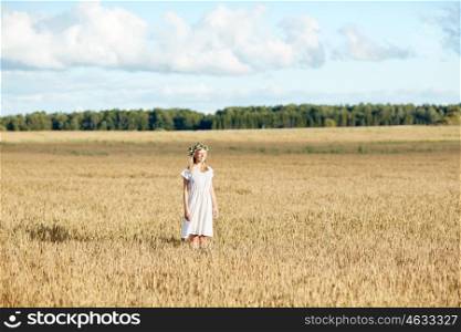 happiness, nature, summer holidays, vacation and people concept - happy smiling young woman or teenage girl in wreath of flowers and white dress on cereal field