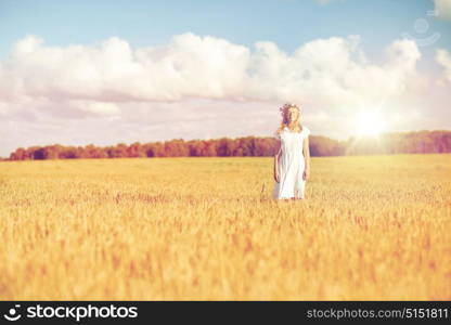 happiness, nature, summer holidays, vacation and people concept - happy smiling young woman or teenage girl in wreath of flowers and white dress on cereal field. happy young woman in flower wreath on cereal field