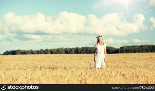 happiness, nature, summer holidays, vacation and people concept - happy smiling young woman or teenage girl in wreath of flowers and white dress on cereal field. happy young woman in flower wreath on cereal field