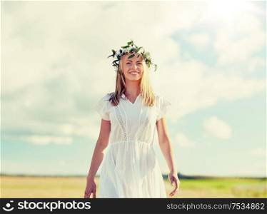 happiness, nature, summer holidays, vacation and people concept - happy smiling young woman or teenage girl in wreath of flowers and white dress at countryside. smiling young woman in wreath of flowers outdoors
