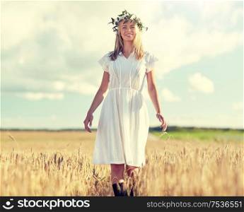 happiness, nature, summer holidays, vacation and people concept - happy smiling young woman or teenage girl in wreath of flowers and white dress on cereal field. happy young woman in flower wreath on cereal field