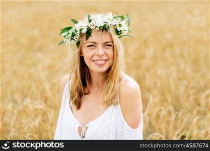 happiness, nature, summer holidays, vacation and people concept - smiling young woman in wreath of flowers on cereal field