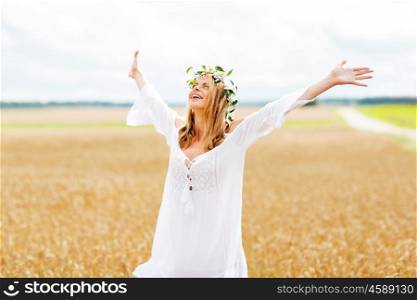 happiness, nature, summer holidays, vacation and people concept - smiling young woman in wreath of flowers and white dress on cereal field