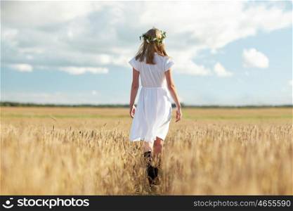 happiness, nature, summer holidays, vacation and people concept - smiling young woman in wreath of flowers and white dress walking along cereal field
