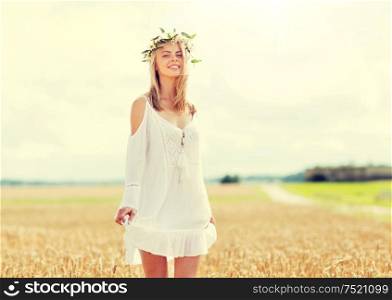 happiness, nature, summer holidays, vacation and people concept - smiling young woman in wreath of flowers and white dress on cereal field. happy young woman in flower wreath on cereal field