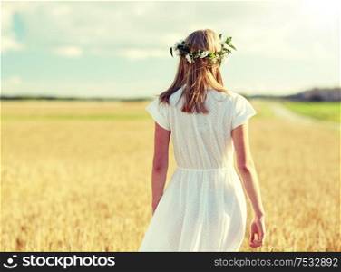 happiness, nature, summer holidays, vacation and people concept - smiling young woman in wreath of flowers and white dress on cereal field. happy young woman in flower wreath on cereal field
