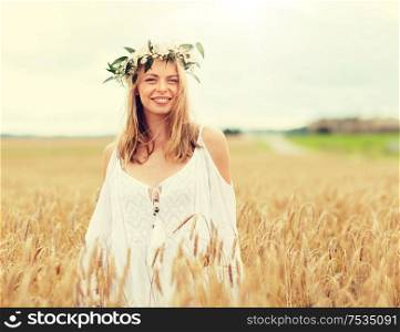 happiness, nature, summer holidays, vacation and people concept - smiling young woman in wreath of flowers on cereal field. happy young woman in flower wreath on cereal field