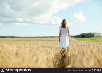 happiness, nature, summer holidays, vacation and people concept - young woman in white dress walking along cereal field