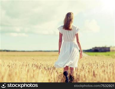 happiness, nature, summer holidays, vacation and people concept - young woman in white dress walking along cereal field. young woman in white dress walking along on field