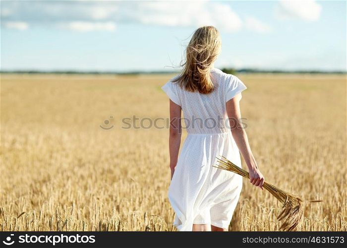 happiness, nature, summer holidays, vacation and people concept - young woman with cereal spikelets walking on field
