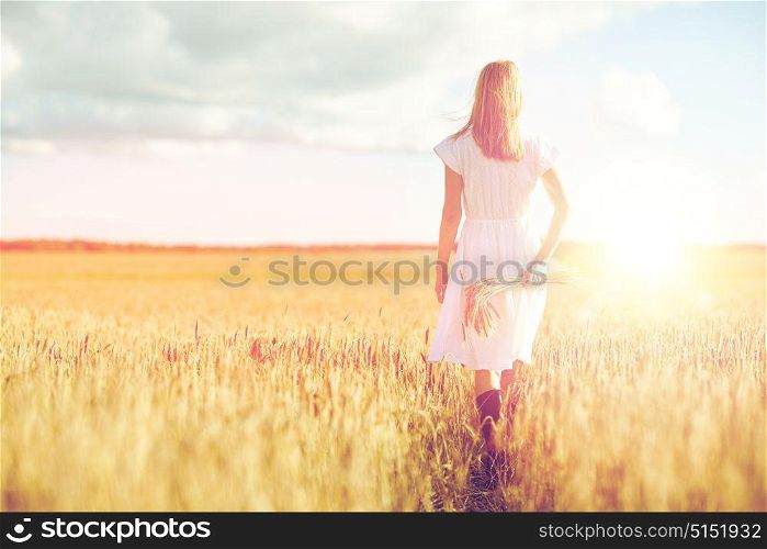 happiness, nature, summer holidays, vacation and people concept - young woman with cereal spikelets walking on field. young woman with cereal spikelets walking on field