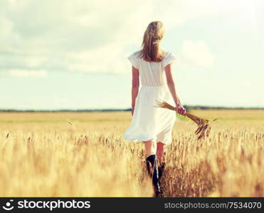 happiness, nature, summer holidays, vacation and people concept - young woman with cereal spikelets walking on field. young woman with cereal spikelets walking on field