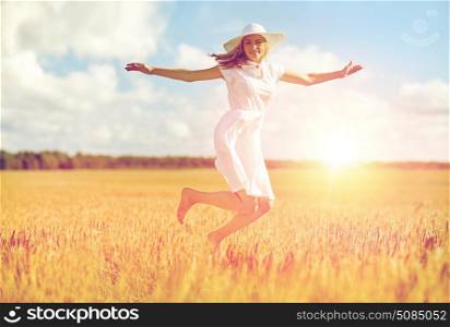 happiness, nature, summer, vacation and people concept - happy smiling young woman or teenage girl wearing straw hat and white dress jumping on cereal field. happy young woman jumping on cereal field. happy young woman jumping on cereal field