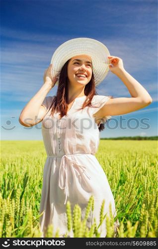happiness, nature, summer, vacation and people concept - smiling young woman wearing straw hat on cereal field