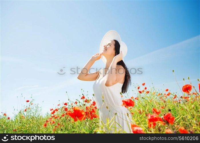 happiness, nature, summer, vacation and people concept - smiling young woman wearing straw hat looking up on poppy field
