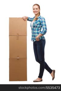 happiness, postal and people concept - smiling young woman standing next to tower of boxes