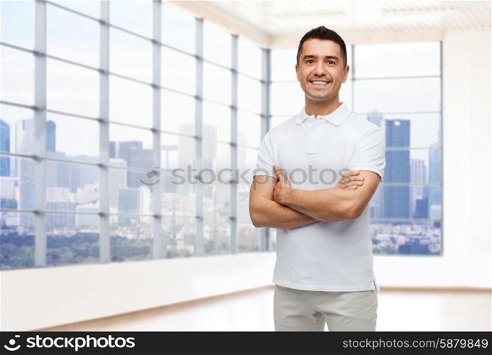 happiness, real estate and people concept - smiling man in white t-shirt over empty apartment or office room with big window and city view background