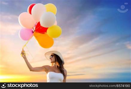 happiness, summer and people concept - smiling young woman wearing sunglasses with balloons over sunset sky background. woman in sunglasses with balloons over sunset sky